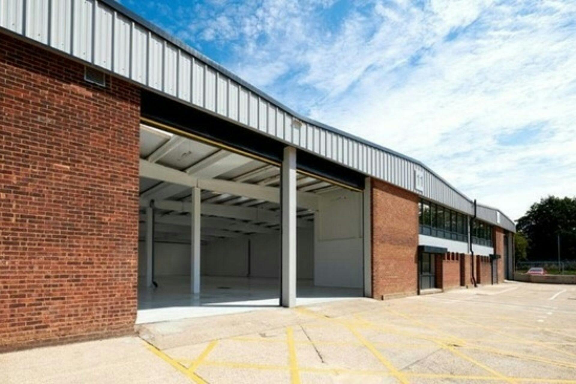 Exterior of an industrial warehouse with large open garage doors and a paved lot under a partly cloudy sky