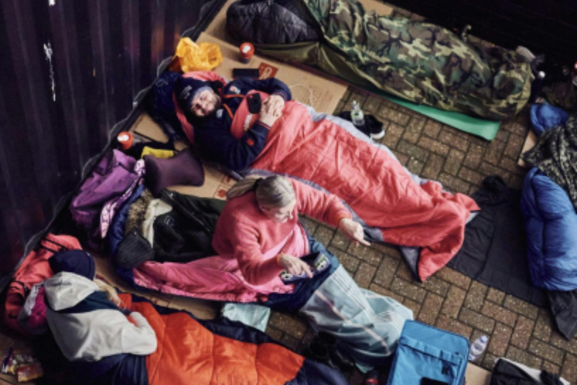 This image depicts a group of people lying on sleeping bags and mats on a brick floor