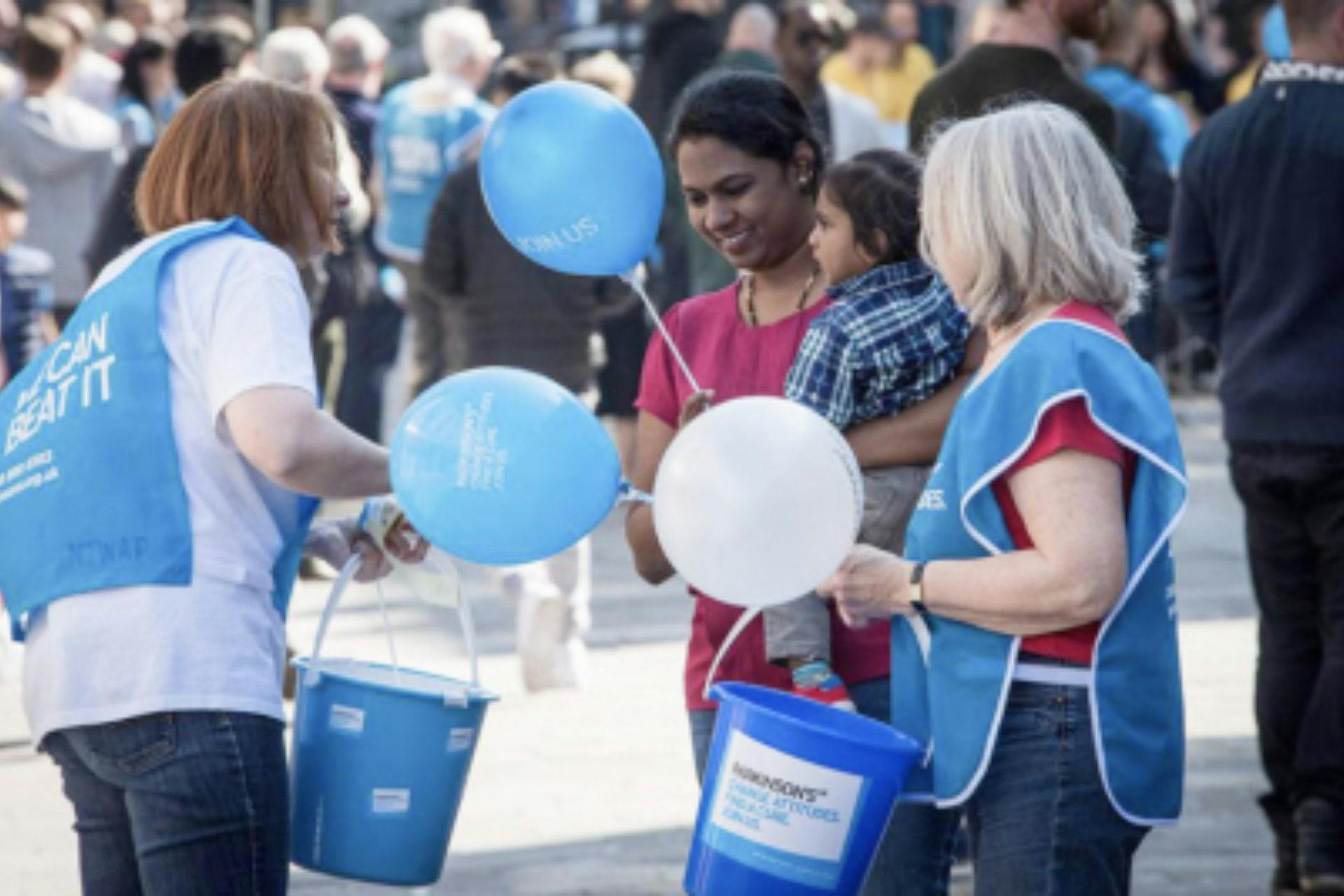 This image shows three individuals engaged in a public charitable activity. Two persons wear blue overalls.